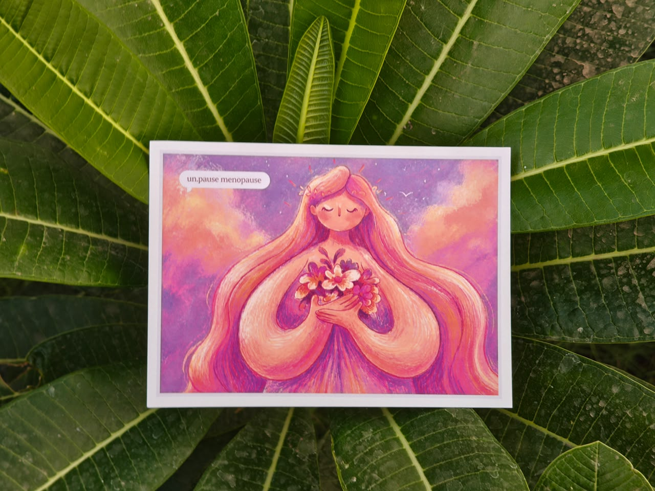 Illustrated un.paused postcard resting on green leaves
